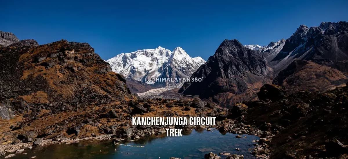 Beautiful Kanchenjunga Circuit Trek landscape showing a snow-covered Mount Kanchenjunga in the background, a snowless mountain around it, and a small lake in the foreground.