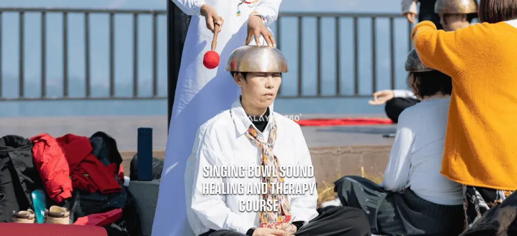 A singing bowl sound healing and therapy class, with a practitioner placing a metal bowl on the head of an individual during the lesson.
